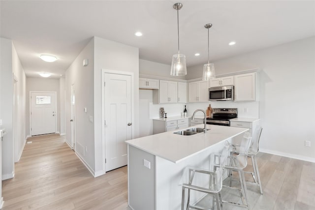 kitchen with stainless steel appliances, sink, a center island with sink, white cabinets, and hanging light fixtures