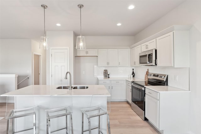 kitchen with appliances with stainless steel finishes, sink, white cabinets, light hardwood / wood-style floors, and an island with sink