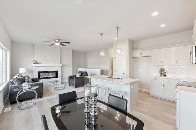 dining area featuring a stone fireplace, ceiling fan, and light hardwood / wood-style floors