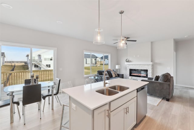 kitchen featuring a fireplace, sink, a center island with sink, light hardwood / wood-style flooring, and dishwasher