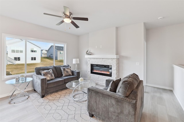 living room with light hardwood / wood-style flooring, a stone fireplace, a wealth of natural light, and ceiling fan