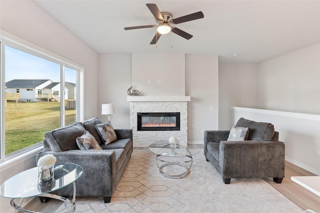 living room with light wood-type flooring, a stone fireplace, and ceiling fan