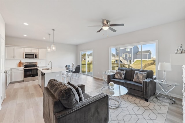 living room featuring ceiling fan, sink, and light wood-type flooring