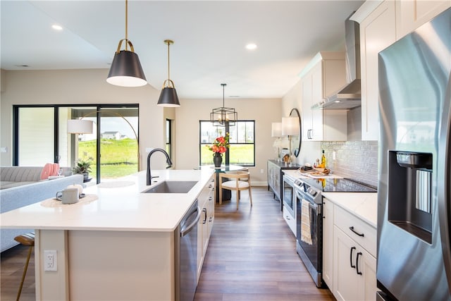 kitchen featuring appliances with stainless steel finishes, tasteful backsplash, sink, a kitchen island with sink, and wall chimney range hood