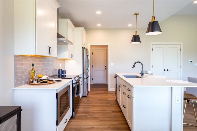 kitchen featuring appliances with stainless steel finishes, decorative backsplash, sink, light wood-type flooring, and a kitchen island with sink