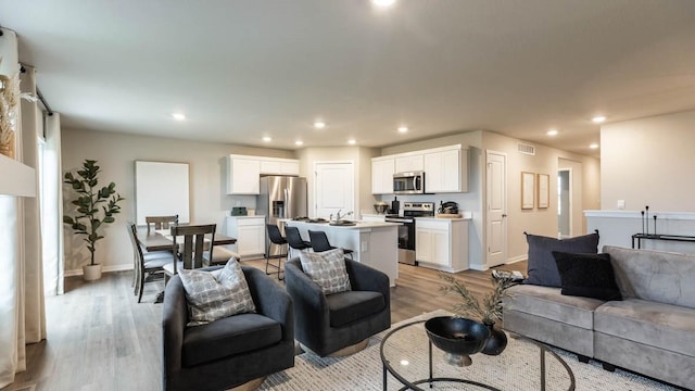 living area with baseboards, light wood-type flooring, visible vents, and recessed lighting