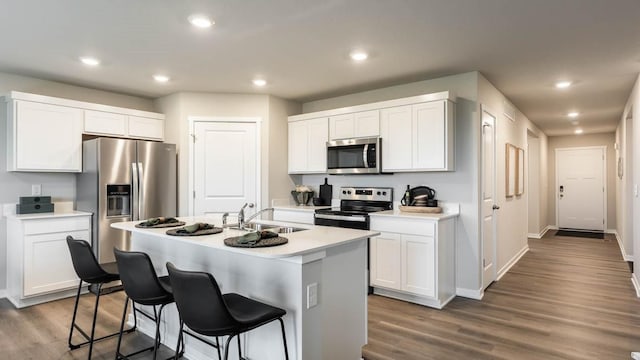 kitchen featuring stainless steel appliances, wood finished floors, a sink, a kitchen breakfast bar, and light countertops