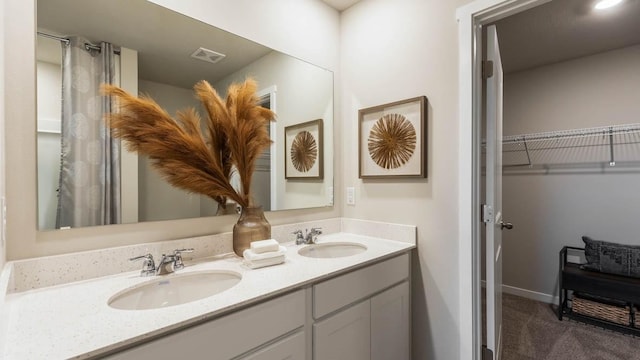 bathroom featuring double vanity, a sink, visible vents, and a walk in closet