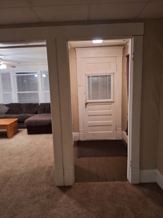 corridor with a paneled ceiling and dark colored carpet