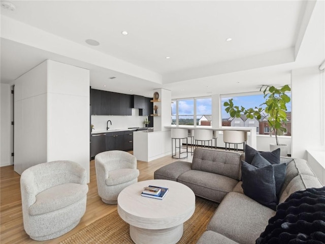 living room with a tray ceiling, sink, and light hardwood / wood-style flooring