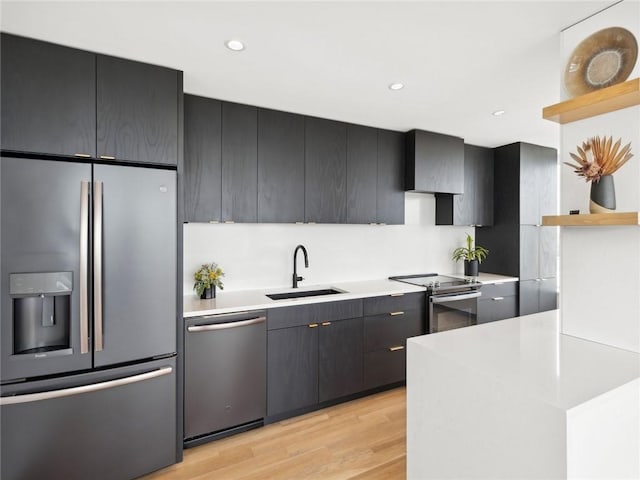 kitchen with appliances with stainless steel finishes, sink, light wood-type flooring, and wall chimney exhaust hood