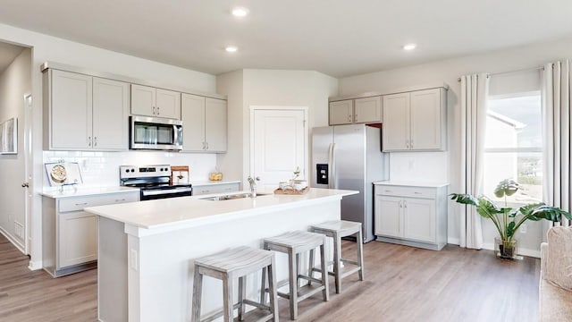 kitchen featuring a breakfast bar area, light wood finished floors, a sink, light countertops, and appliances with stainless steel finishes