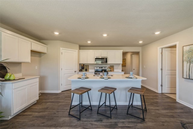 kitchen with dark wood-type flooring, white cabinetry, stainless steel appliances, and a center island with sink