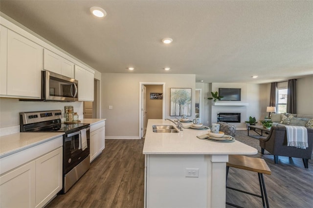 kitchen with an island with sink, sink, white cabinetry, appliances with stainless steel finishes, and dark hardwood / wood-style flooring