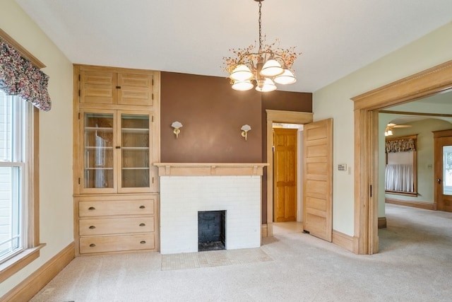 unfurnished living room featuring a chandelier, light carpet, and a brick fireplace