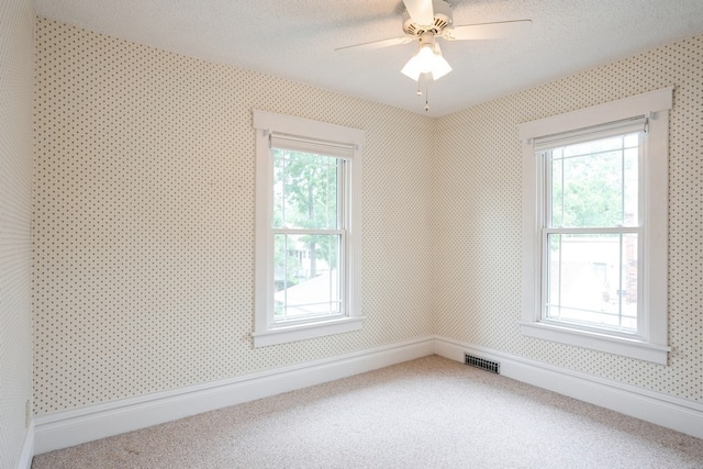 empty room featuring a textured ceiling, carpet floors, ceiling fan, and a healthy amount of sunlight