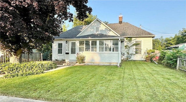 view of front of property featuring fence, a sunroom, a shingled roof, a chimney, and a front lawn