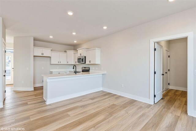 kitchen with kitchen peninsula, sink, white cabinets, and light hardwood / wood-style floors