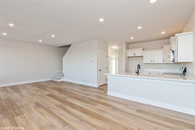 kitchen with light wood-type flooring, a textured ceiling, sink, stainless steel range oven, and white cabinets