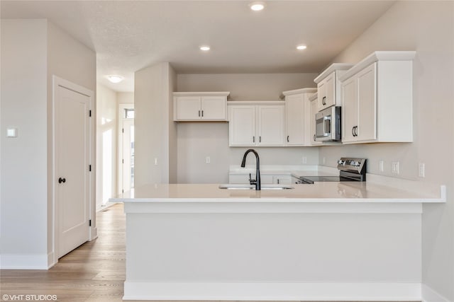 kitchen featuring kitchen peninsula, appliances with stainless steel finishes, sink, light hardwood / wood-style floors, and white cabinetry