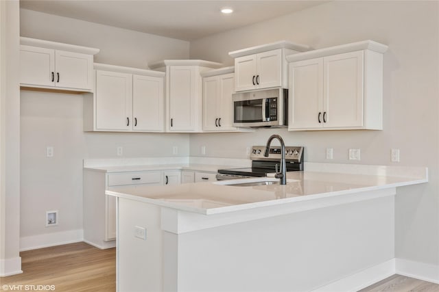 kitchen featuring white cabinets, stainless steel appliances, kitchen peninsula, and light hardwood / wood-style flooring