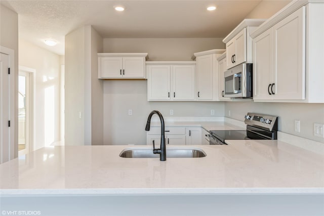 kitchen with white cabinets, stainless steel appliances, light stone counters, and sink