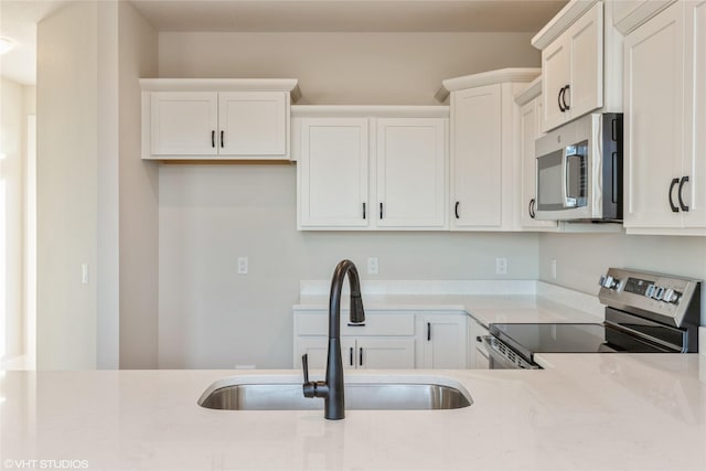 kitchen with light stone countertops, appliances with stainless steel finishes, white cabinetry, and sink