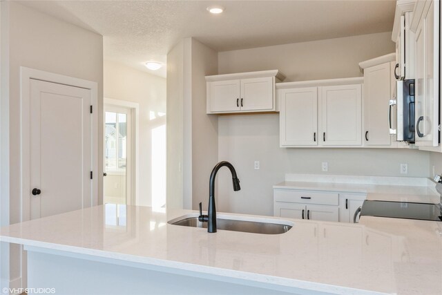 kitchen featuring stove, white cabinets, sink, light stone countertops, and a textured ceiling