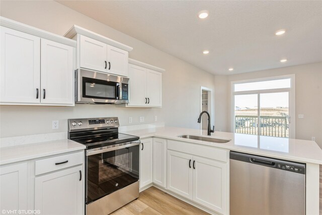 kitchen with sink, light hardwood / wood-style flooring, kitchen peninsula, white cabinets, and appliances with stainless steel finishes