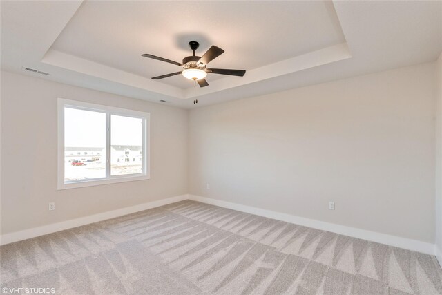 empty room with carpet floors, a raised ceiling, and ceiling fan