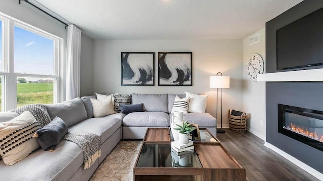 living room with a glass covered fireplace, visible vents, baseboards, and wood finished floors