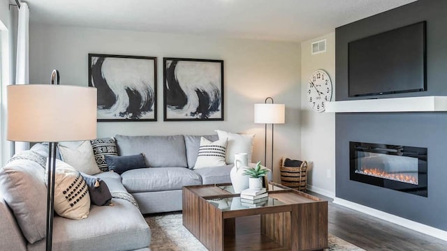 living room with a glass covered fireplace, visible vents, baseboards, and wood finished floors