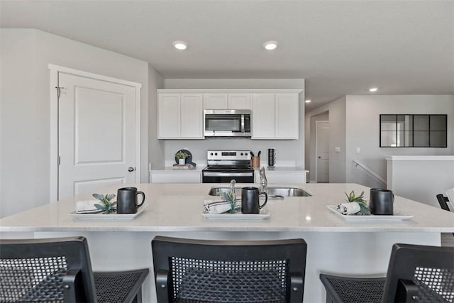 kitchen with sink, a breakfast bar area, stainless steel appliances, a kitchen island with sink, and white cabinets