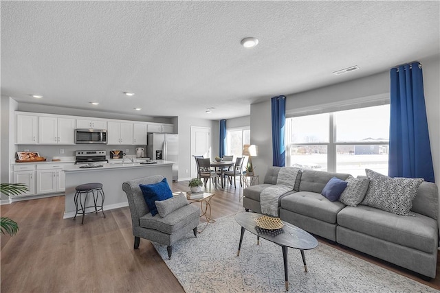 living room with recessed lighting, a textured ceiling, visible vents, and wood finished floors