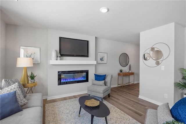 living room featuring a glass covered fireplace, baseboards, and wood finished floors