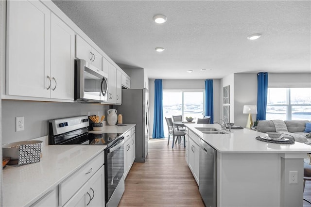 kitchen with white cabinets, stainless steel appliances, a textured ceiling, and an island with sink