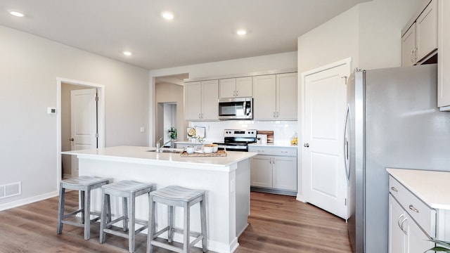 kitchen with hardwood / wood-style flooring, stainless steel appliances, a breakfast bar area, decorative backsplash, and a center island with sink