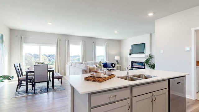 kitchen with a kitchen island with sink, dishwasher, light stone counters, sink, and light hardwood / wood-style floors