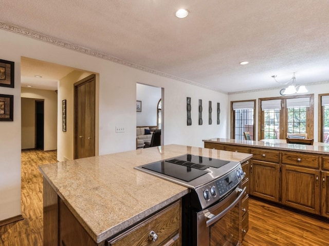 kitchen featuring electric stove, light stone counters, a kitchen island, a textured ceiling, and hardwood / wood-style flooring