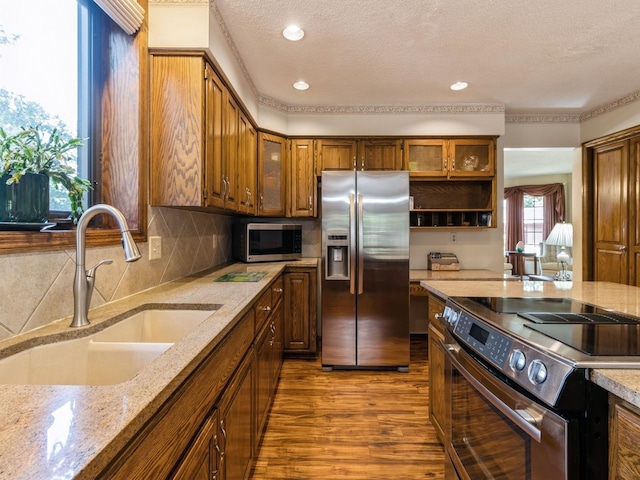 kitchen with sink, backsplash, light stone counters, stainless steel appliances, and hardwood / wood-style flooring