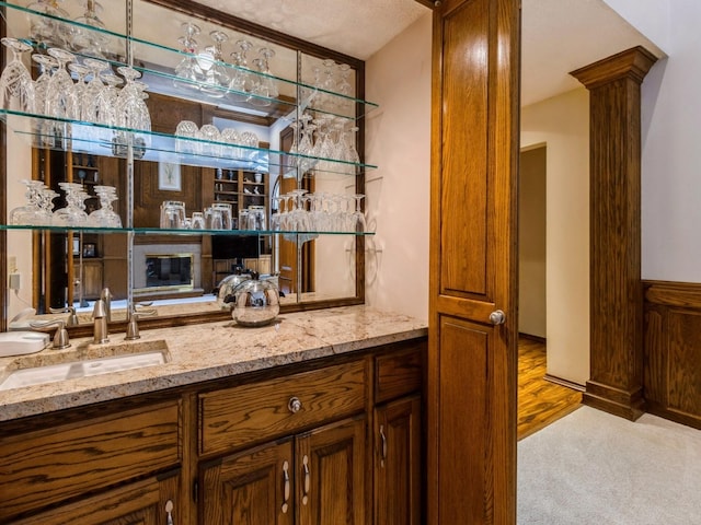 bar featuring sink, light carpet, decorative columns, and light stone counters