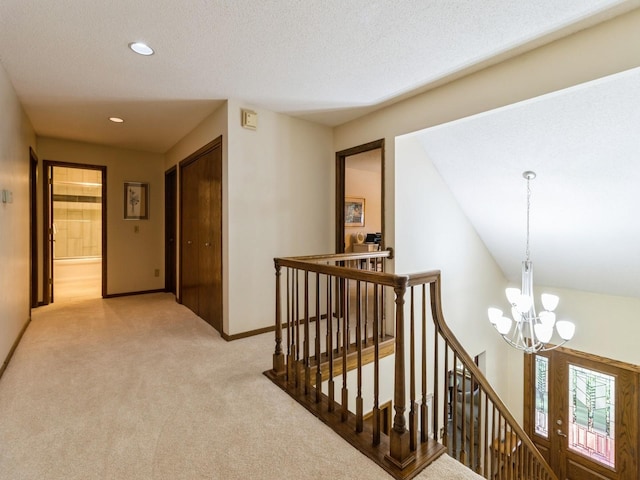 corridor with an inviting chandelier, a textured ceiling, and light colored carpet