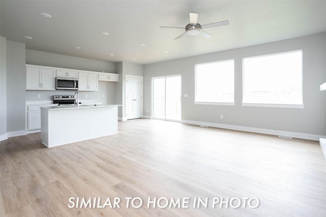 kitchen with a center island with sink, light wood-style flooring, white cabinets, baseboards, and appliances with stainless steel finishes