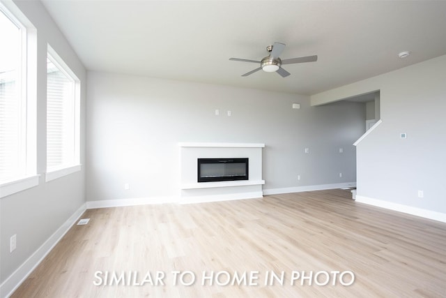 unfurnished living room featuring ceiling fan, baseboards, a glass covered fireplace, and light wood-style floors