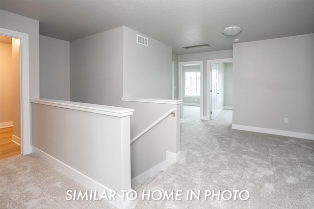 hall with carpet, visible vents, baseboards, and an upstairs landing