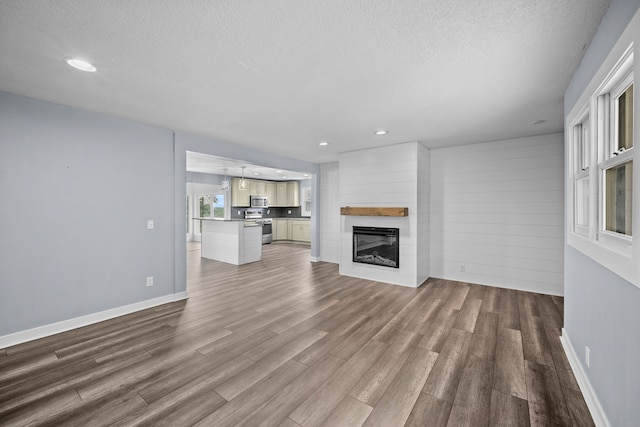 unfurnished living room featuring a textured ceiling, wooden walls, a large fireplace, and wood-type flooring