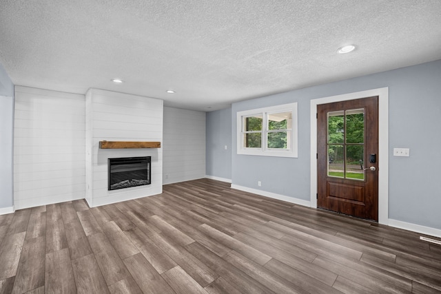 unfurnished living room featuring a large fireplace, a textured ceiling, and wood finished floors