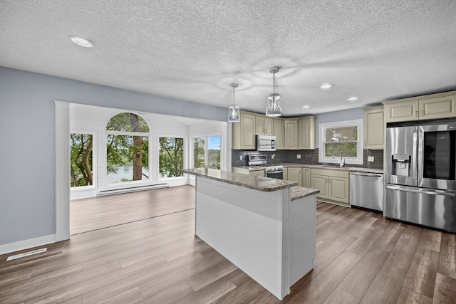 kitchen featuring decorative light fixtures, light wood finished floors, stainless steel appliances, backsplash, and stone countertops