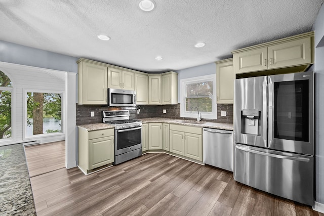 kitchen with appliances with stainless steel finishes, hardwood / wood-style flooring, sink, and decorative backsplash