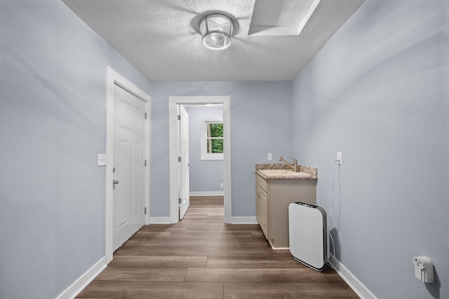 hallway with a textured ceiling, a sink, wood finished floors, and baseboards